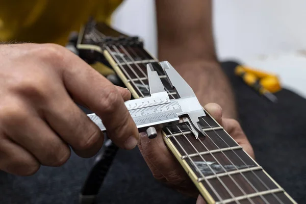 Latin Amerikalı Luthier bir elektro gitarın tellerini bir vernier ile doğru olarak kalibre eder. Tanımlanamayan kişi. Gitar konsepti, kalibrasyon, alet.