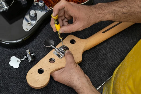 Latin Amerikalı Luthier 'in elleri bir tornavidayla elektrikli levrek sapını yerleştirip ayarlıyor. Tanımlanamayan kişi. Kavram onarımı, enstrüman, bas