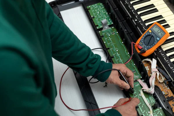 Hands of Latin American electronic technician with a multimeter makes current and resistance measurements to an electronic board of an electric piano in a service center. Repair concept, piano, electronics
