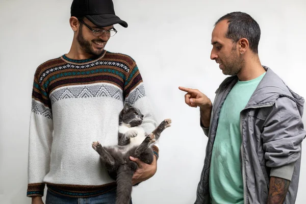 Latin American male couple standing play with their cat while giving her love and cuddles. White background. Pets Concept