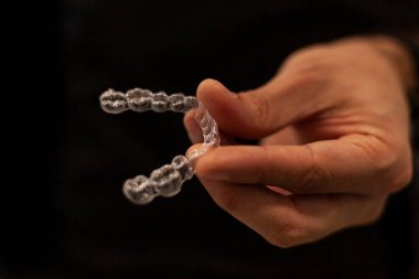 Elinde görünmez bir hizalayıcı tutan bir ortodonti uzmanının yakın çekimi. Görünmez ortodonti tekniği kavramı.