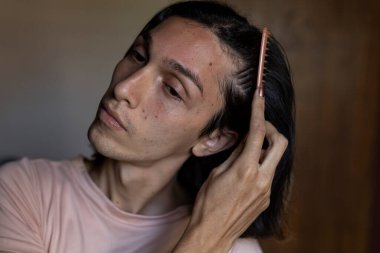 Genç transseksüel (22) adam saçını tarıyor. Transseksüel Konsepti