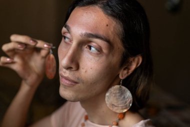 Genç travesti (22) odasında aksesuarlarını takıyor. Transseksüel Konsepti