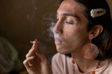 Genç bir travesti (22) odasında sigara içiyor ve ağzından çıkan dumanı görebilirsiniz. Transseksüel kavramı