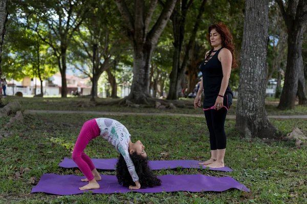 Latin American mom and daughter have fun in the park doing yoga and exercise together