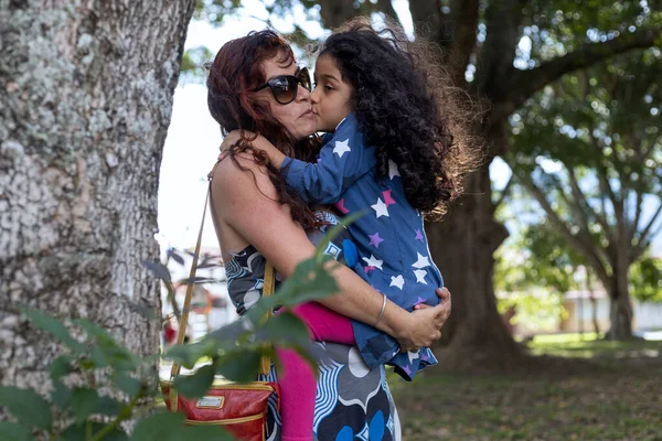 Mom and her Latina daughter share together in the park, she holds her daughter in her arms lovingly