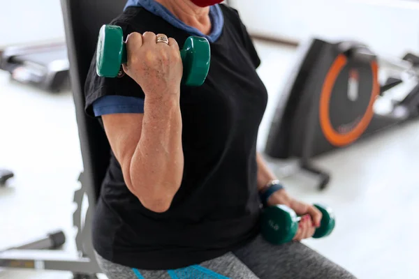 Elderly Latina woman works out with dumbbells at the gym