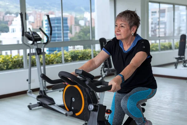 Older Latina woman works out at the gym using the workout machines