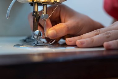 Latin American seamstress inserts thread into sewing machine needle