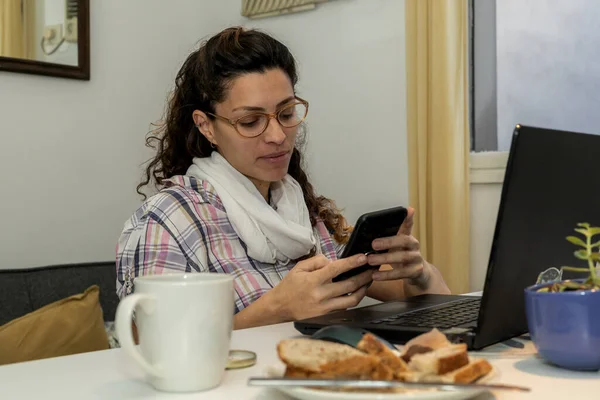 latin american woman takes a break and eats something while working from home