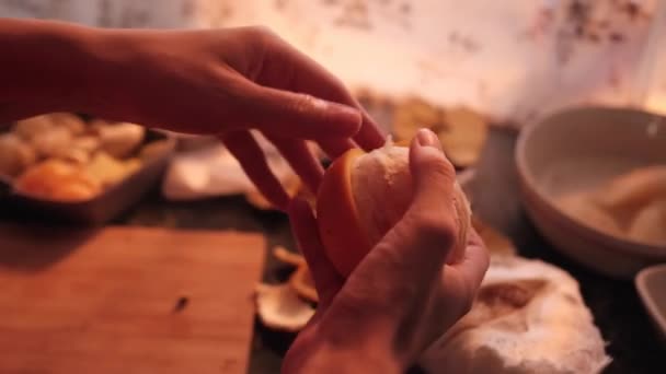 Flickan skalar en apelsin med händerna i köket — Stockvideo