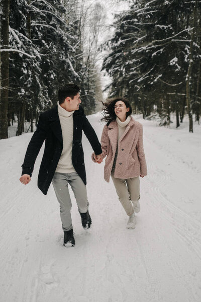 A happy young couple runs along the road in a snowy forest. High quality photo