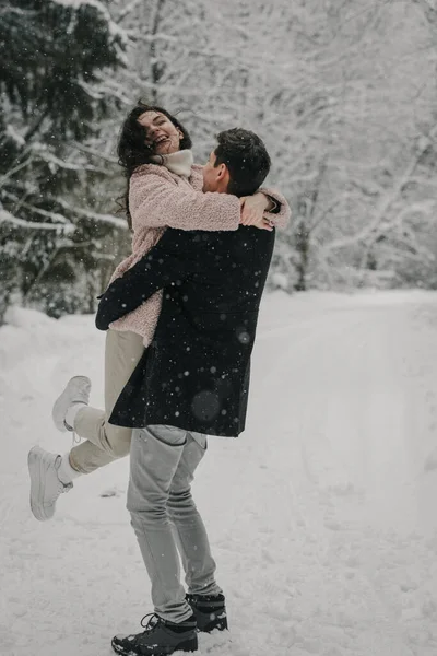 Um jovem casal feliz está girando na estrada em uma floresta nevada — Fotografia de Stock