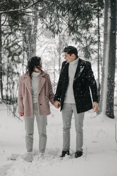 Um casal milenar apaixonado está de pé sob uma árvore da qual a neve está caindo — Fotografia de Stock