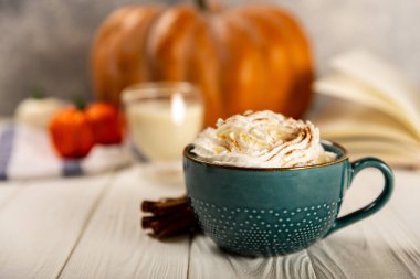 Lezzetli, aromatik latte, balkabağı ve tarçınlı mavi bir fincanda, beyaz arka planda bir ağaçla..