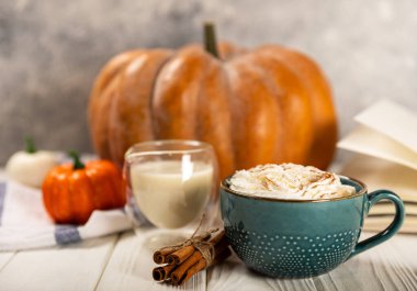 Lezzetli, aromatik latte, balkabağı ve tarçınlı mavi bir fincanda, beyaz arka planda bir ağaçla..