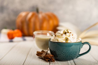 Lezzetli, aromatik latte, balkabağı ve tarçınlı mavi bir fincanda, beyaz arka planda bir ağaçla..