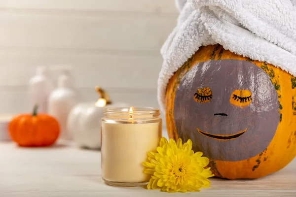 Pumpkins with face mask and towel on white background, burning candle, cosmetics with copy space