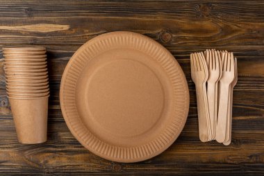 Çevre dostu tek kullanımlık kağıt sofra takımı. Kağıt bardak, tahta çatal, tahta arka planda kağıt tabak. Geri dönüşüm veya yeşil kavram.
