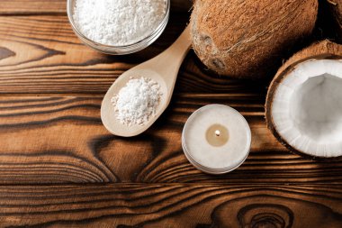 Tahta bir kaşıkta hindistan cevizi taneleri ve bir kasede hindistan cevizleri, ahşap bir zeminde beyaz bir mum. Yakın plan. Boşluğu kopyala.