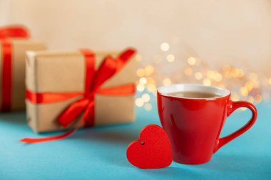Hediye kutusu, kırmızı kalp ve mavi arka planda bir fincan kırmızı çay. Sevgililer günü hediyesi. Tatiller ve aşk konsepti.