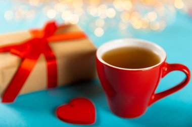 Hediye kutusu, kırmızı kalp ve mavi arka planda bir fincan kırmızı çay. Sevgililer günü hediyesi. Tatiller ve aşk konsepti.