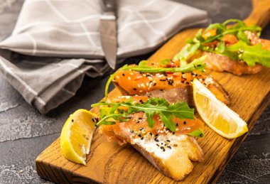 Lezzetli bruschetta ya da somonlu kanepe. Tuzlu somon, roka ve ahşap tahtada krem peynirli sandviç..