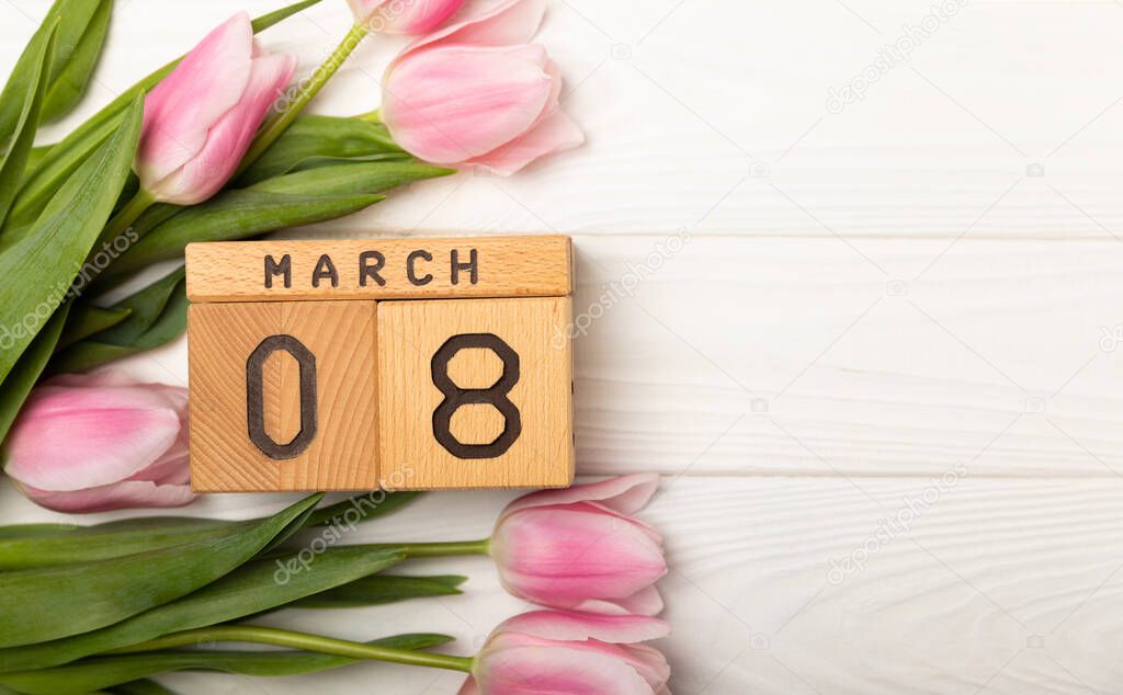 International Women's Day.Beautiful card for March 8.Spring bouquet of pink tulips with a wooden calendar on a white textured wood. Holiday concept.Copy space.