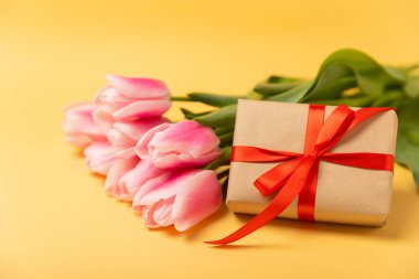 Pembe laleler ve sarı arka planda bir hediye kutusu. Bahar buketi. Bayram konsepti. Kadınlar günü, Sevgililer günü, Paskalya, doğum günü..