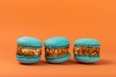 Turuncu arka planda Fransız kurabiyeleri. Mavi ve armutlu makarnalar. Fransız tatlısı. Güzel masa. Boşluğu kopyala. Mesaj için yer.