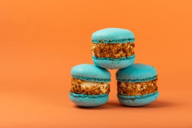 Turuncu arka planda Fransız kurabiyeleri. Mavi ve armutlu makarnalar. Fransız tatlısı. Güzel masa. Boşluğu kopyala. Mesaj için yer.