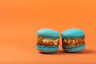 Turuncu arka planda Fransız kurabiyeleri. Mavi ve armutlu makarnalar. Fransız tatlısı. Güzel masa. Boşluğu kopyala. Mesaj için yer.