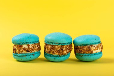 Sarı arka planda Fransız kurabiyeleri. Mavi ve armutlu makarnalar. Fransız tatlısı. Güzel masa. Boşluğu kopyala. Mesaj için yer.