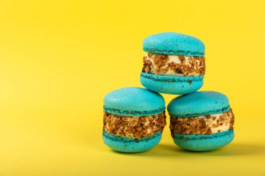 Sarı arka planda Fransız kurabiyeleri. Mavi ve armutlu makarnalar. Fransız tatlısı. Güzel masa. Boşluğu kopyala. Mesaj için yer.