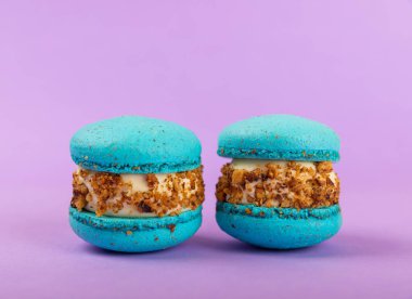 Leylak arkaplanlı Fransız kurabiyeleri. Mavi ve armutlu makarnalar. Fransız tatlısı. Güzel masa. Boşluğu kopyala. Mesaj için yer.