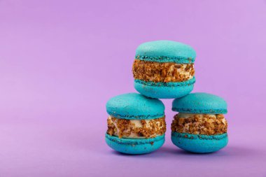 Leylak arkaplanlı Fransız kurabiyeleri. Mavi ve armutlu makarnalar. Fransız tatlısı. Güzel masa. Boşluğu kopyala. Mesaj için yer.