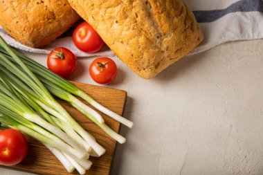 Yeşil soğan, ev yapımı ekmek ve gri taştan arka planda kiraz domatesleri. Taze sebzeler. Vitaminler. Boşluğu kopyala. Metin için yer.