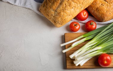 Yeşil soğan, ev yapımı ekmek ve gri taştan arka planda kiraz domatesleri. Taze sebzeler. Vitaminler. Boşluğu kopyala. Metin için yer.