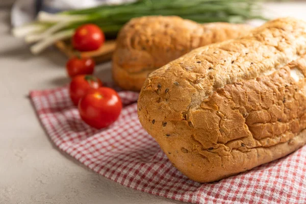 Taze ev yapımı ekmek, yeşil soğanlı ve gri çimento arka planda mutfak havlusunda kiraz domatesli. Keten tohumlu ekmek, ayçiçeği tohumu ve ekşi ekmek. Organik ev yapımı hamur işleri.. 