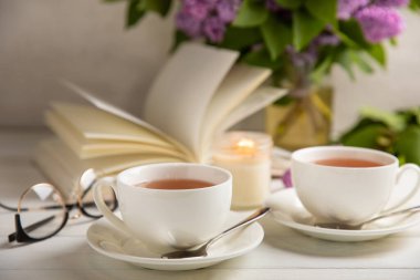 Bir fincan yeşil çay, arka planda bir demet leylağın üzerine serpiştirilmiş gri bir arkaplan. Kitaplar ve mumlarla romantik kompozisyon. Bahar çayı içeceği. Yan görüş. Kopyalanacak yer.