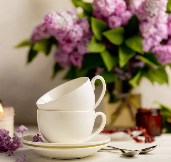 Tea set against the background of a spring bouquet of lilacs on a textured gray background. Composition with books and candles. Side view. Place to copy.
