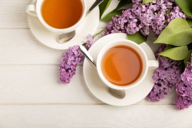 Bir fincan yeşil çay, arka planda bir demet leylağın üzerine serpiştirilmiş gri bir arkaplan. Kitaplar ve mumlarla romantik kompozisyon. Bahar çayı içeceği. Kopyalanacak yer.