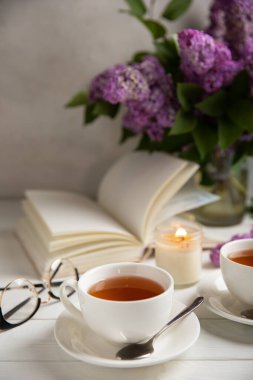 Bir fincan yeşil çay, arka planda bir demet leylağın üzerine serpiştirilmiş gri bir arkaplan. Kitaplar ve mumlarla romantik kompozisyon. Bahar çayı içeceği. Yan görüş. Kopyalanacak yer.
