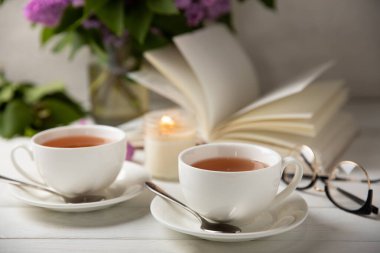 Bir fincan yeşil çay, arka planda bir demet leylağın üzerine serpiştirilmiş gri bir arkaplan. Kitaplar ve mumlarla romantik kompozisyon. Bahar çayı içeceği. Yan görüş. Kopyalanacak yer.