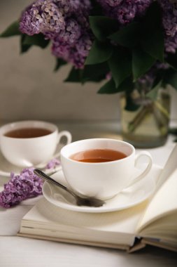 Bir fincan yeşil çay, arka planda bir demet leylağın üzerine serpiştirilmiş gri bir arkaplan. Kitaplar ve mumlarla romantik kompozisyon. Bahar çayı içeceği. Yan görüş. Kopyalanacak yer.