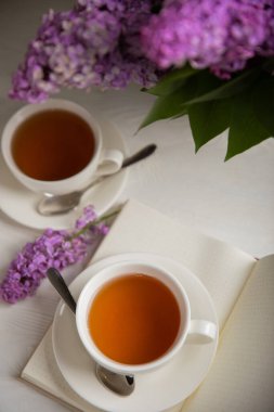 Bir fincan yeşil çay, arka planda bir demet leylağın üzerine serpiştirilmiş gri bir arkaplan. Kitaplar ve mumlarla romantik kompozisyon. Bahar çayı içeceği. Yan görüş. Kopyalanacak yer.