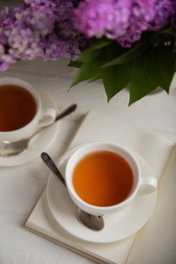 Bir fincan yeşil çay, arka planda bir demet leylağın üzerine serpiştirilmiş gri bir arkaplan. Kitaplar ve mumlarla romantik kompozisyon. Bahar çayı içeceği. Yan görüş. Kopyalanacak yer.