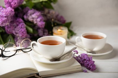 Bir fincan yeşil çay, arka planda bir demet leylağın üzerine serpiştirilmiş gri bir arkaplan. Kitaplar ve mumlarla romantik kompozisyon. Bahar çayı içeceği. Yan görüş. Kopyalanacak yer.