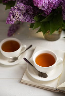 Bir fincan yeşil çay, arka planda bir demet leylağın üzerine serpiştirilmiş gri bir arkaplan. Kitaplar ve mumlarla romantik kompozisyon. Bahar çayı içeceği. Yan görüş. Kopyalanacak yer.