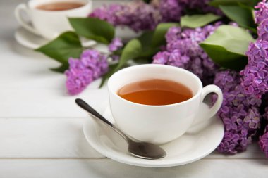 Bir fincan yeşil çay, arka planda bir demet leylağın üzerine serpiştirilmiş gri bir arkaplan. Kitaplar ve mumlarla romantik kompozisyon. Bahar çayı içeceği. Kopyalanacak yer.